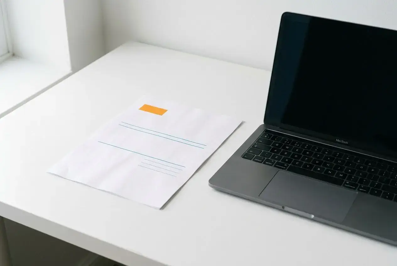 Classeur et ordinateur portable sur une table blanche, affichant une scène de travail autour d’une facture pro forma.